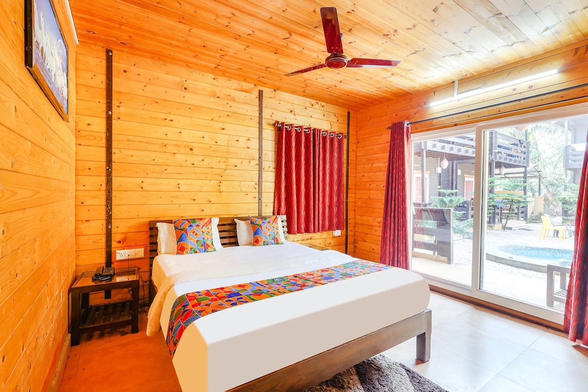 Dormitorio de cabaña de madera con cama, ventilador de techo y vista al exterior.