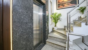 A modern elevator, a staircase with metal railings, and a framed landscape painting on the wall. - Fabhotel Ak Villa (New Delhi)