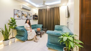 A living room with a sofa, two potted plants, a coffee table, and a ceiling fan. - Fabhotel Ak Villa (New Delhi)