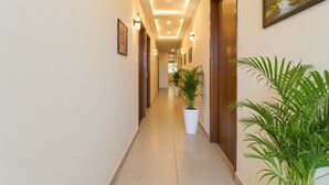 A hotel hallway with a tiled floor, potted plants, framed artwork on the walls, and recessed lighting. - Fabhotel Lfc (Jaipur)