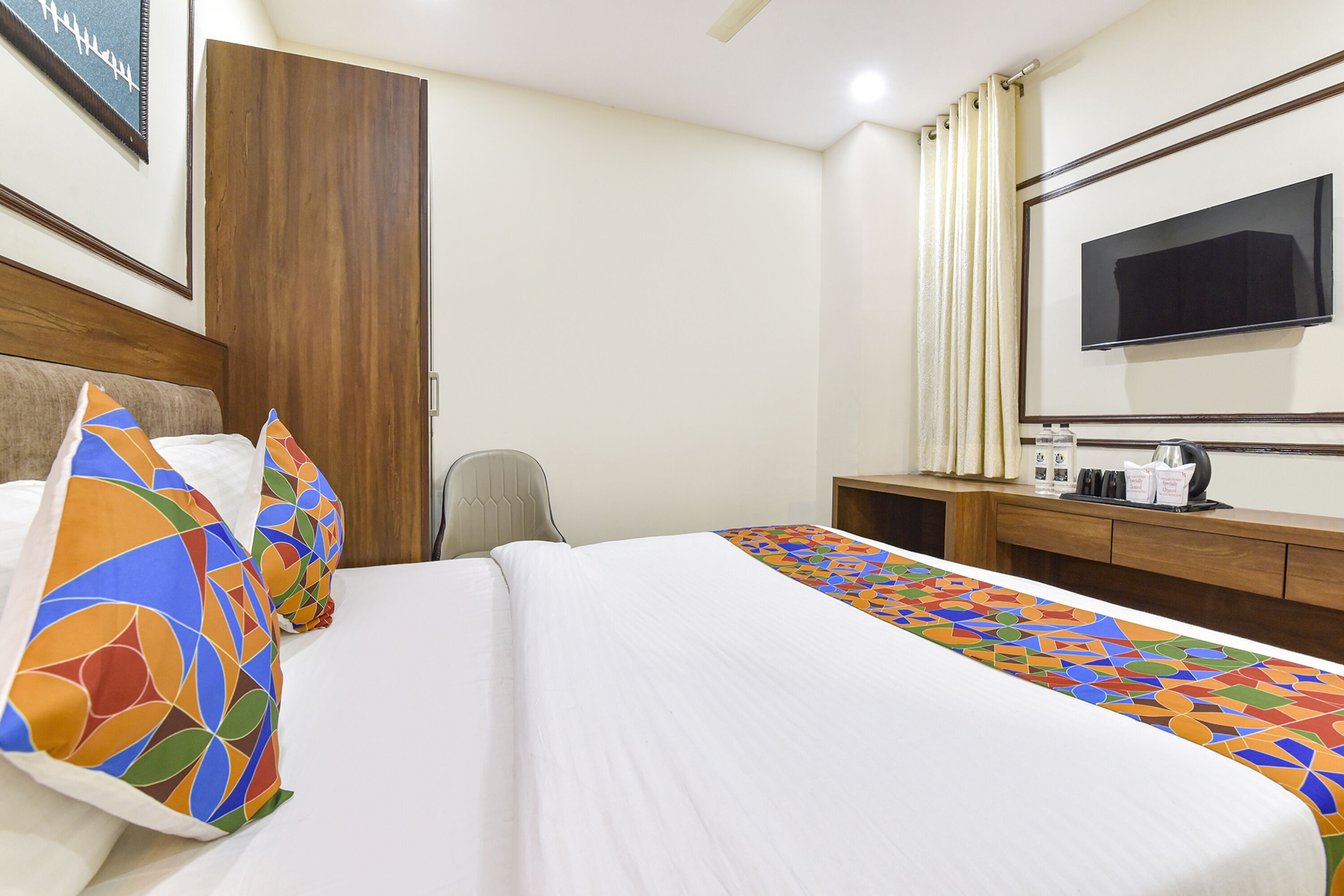 A hotel room with a bed, a desk, a chair, a television, and a wardrobe.