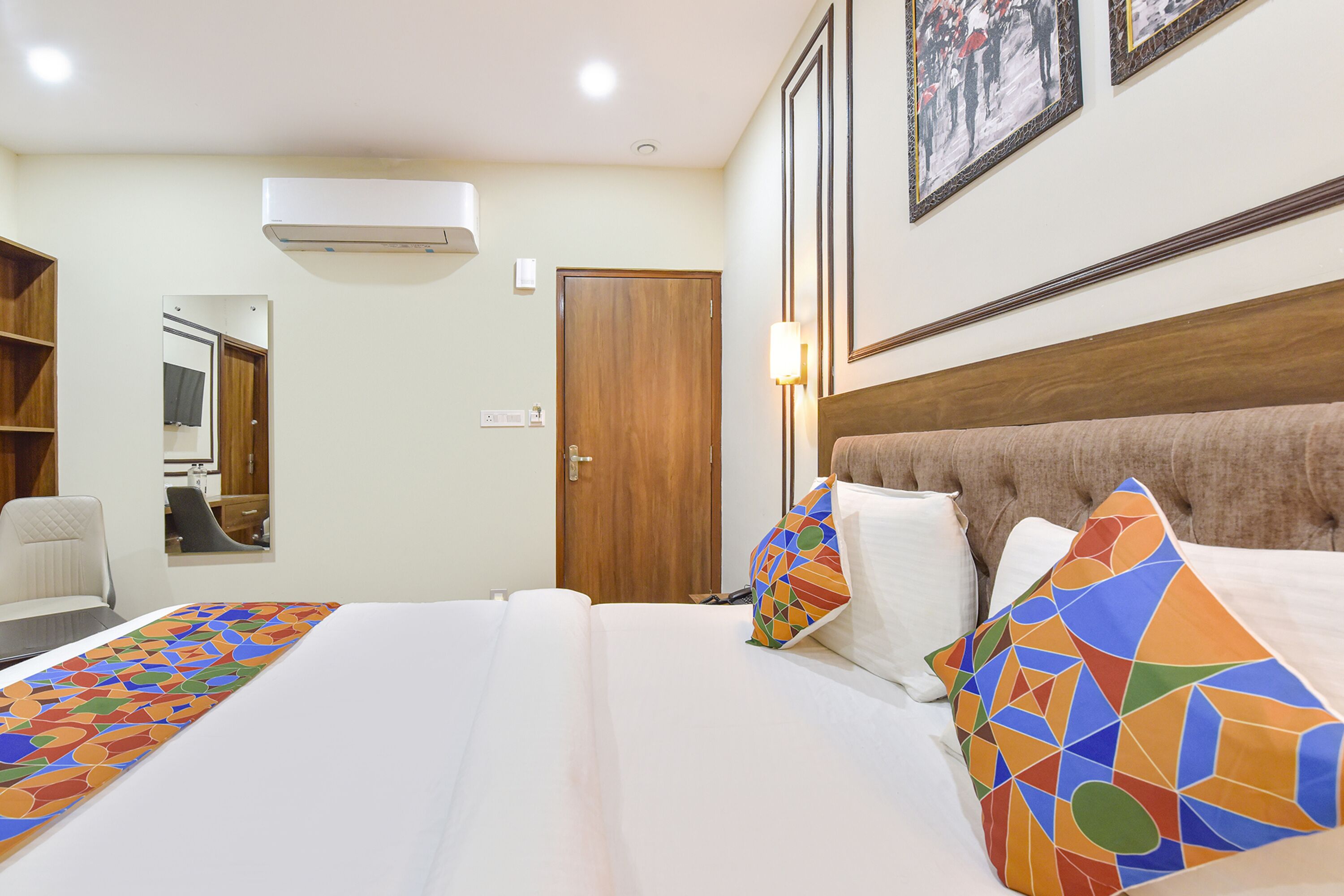 Habitación de hotel con una cama grande, cabecera de madera, un espejo, un equipo de aire acondicionado y una puerta.