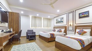 A hotel room with two beds, a desk, a chair, a ceiling fan, and artwork on the walls. - Fabhotel Lfc (Jaipur)