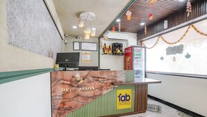 A reception desk with a 'fab hotels' sign, a Coca-Cola refrigerator, and a wall-mounted air conditioner.