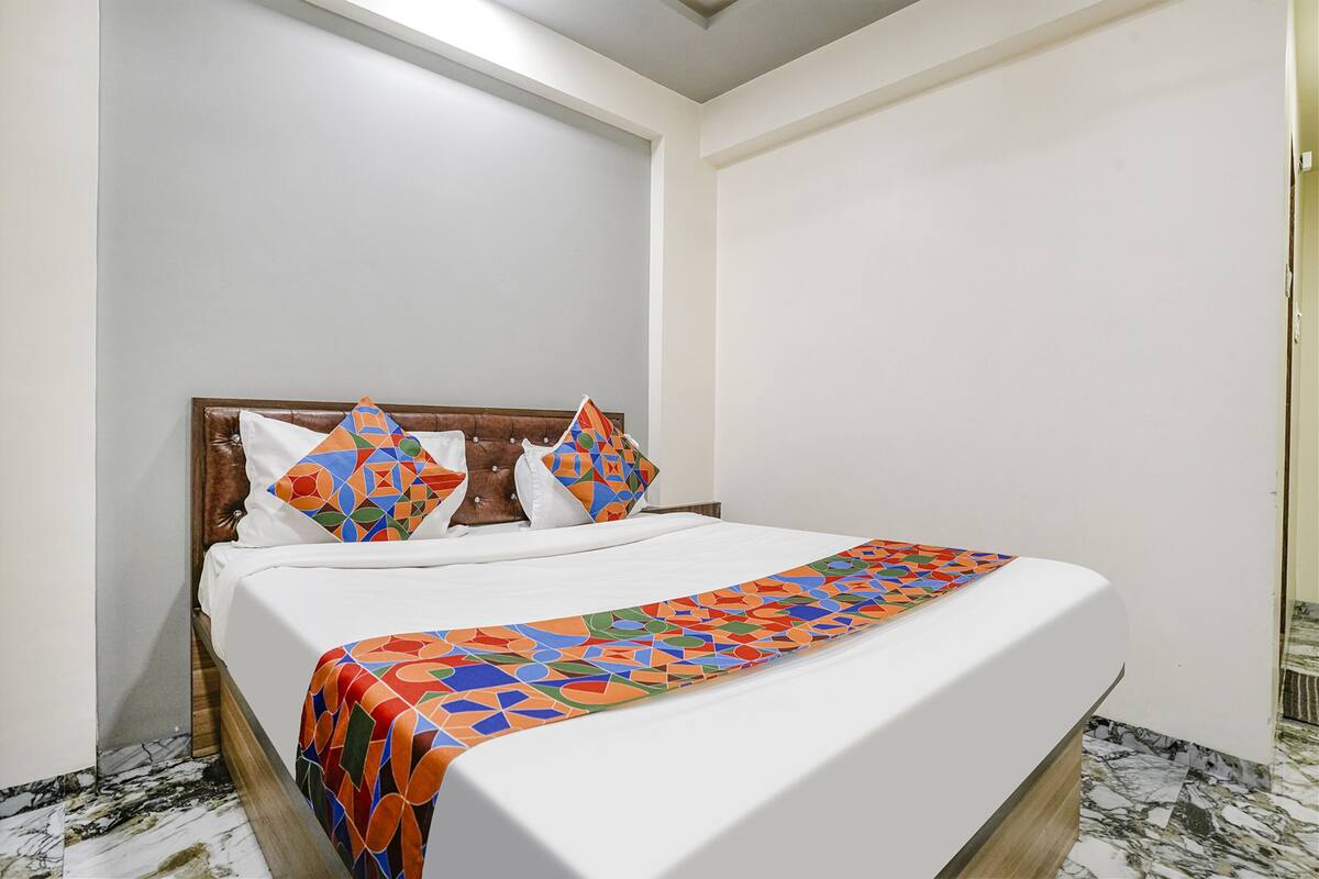 Un letto rifatto con cura, coperto da una trapunta decorata e cuscini, una testiera in legno e un pavimento in marmo.