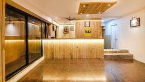 A hotel reception area with a wooden reception desk, a clock, and framed pictures on the wall.