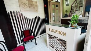 A reception area with a reception desk, a red chair, and a sign indicating the checkout time. - Fabhotel Purvika (Varanasi)