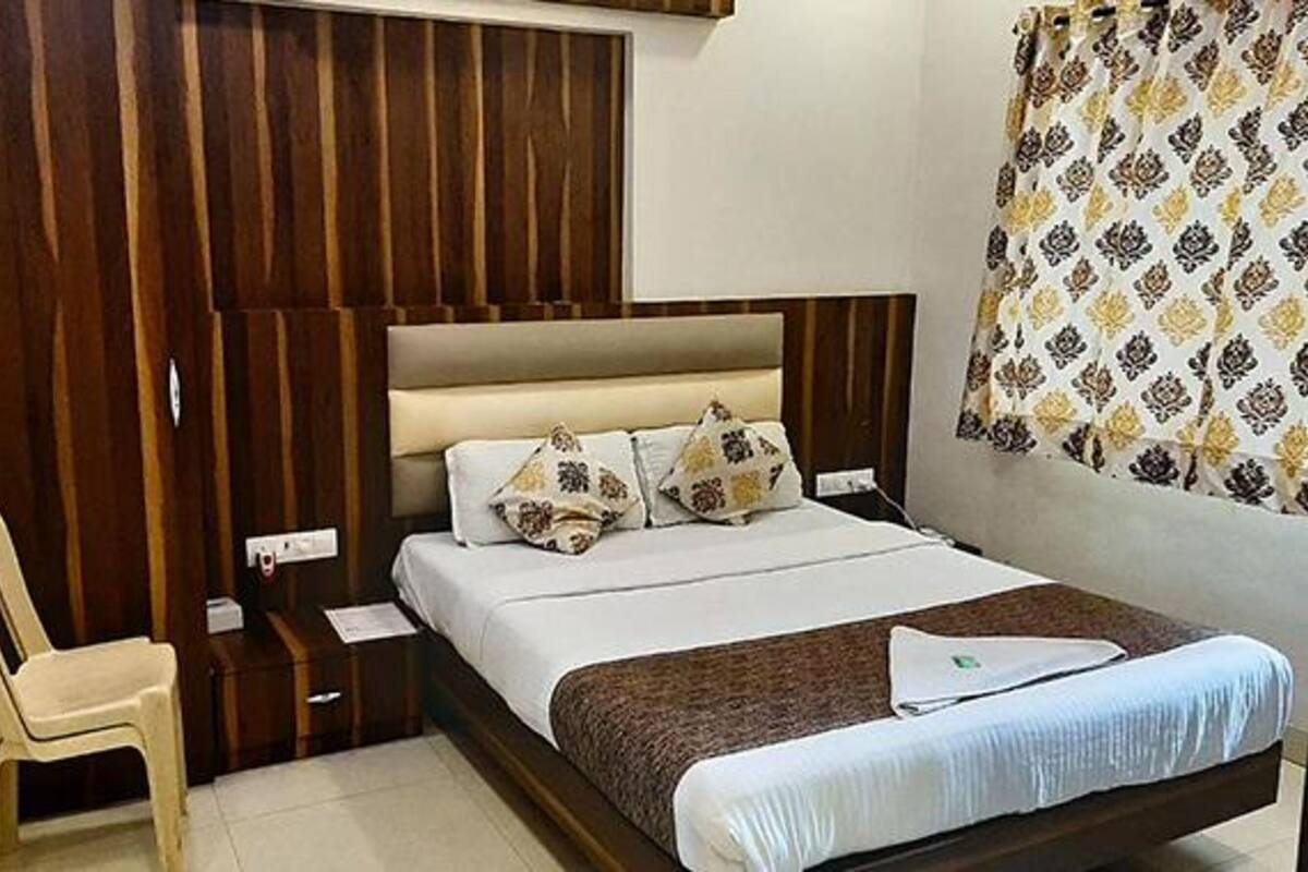 A bedroom with a wooden headboard, a bed with white bedding and patterned pillows, a bedside table, and a chair.