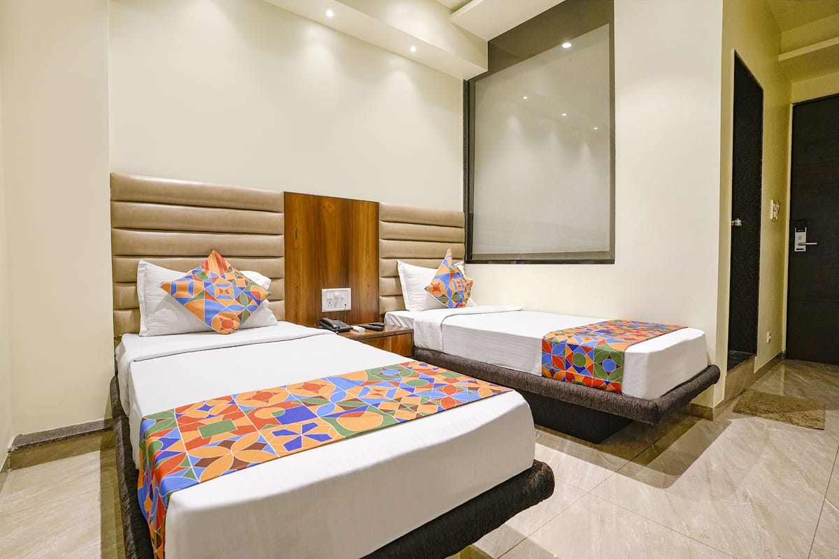 A hotel room with two beds, each with a colorful geometric-patterned bedspread, a wooden headboard, and a large window.