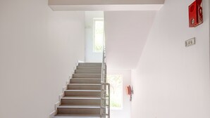 A staircase leading to a bright room with a window, a red fire alarm, and a white wall. - FabHotel Noronha Goaxa Inn - Nr. Calangute beach (Calangute)