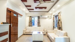 A modern living room with a sofa, a coffee table, a ceiling fan, and a door labeled "WASHROOM". - FabHotel Noronha Goaxa Inn - Nr. Calangute beach (Calangute)