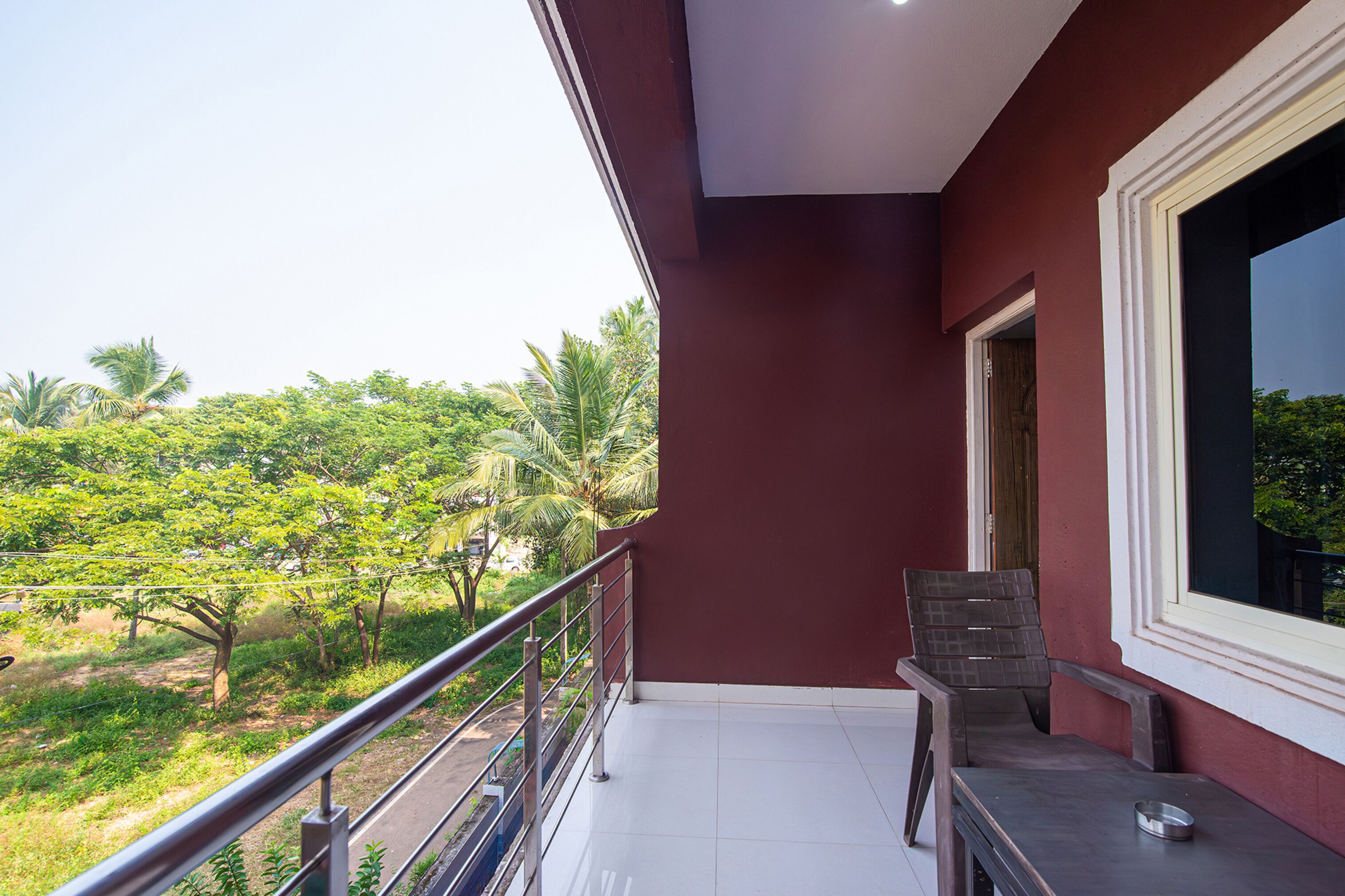 A balcony with a view of greenery and a red wall.
