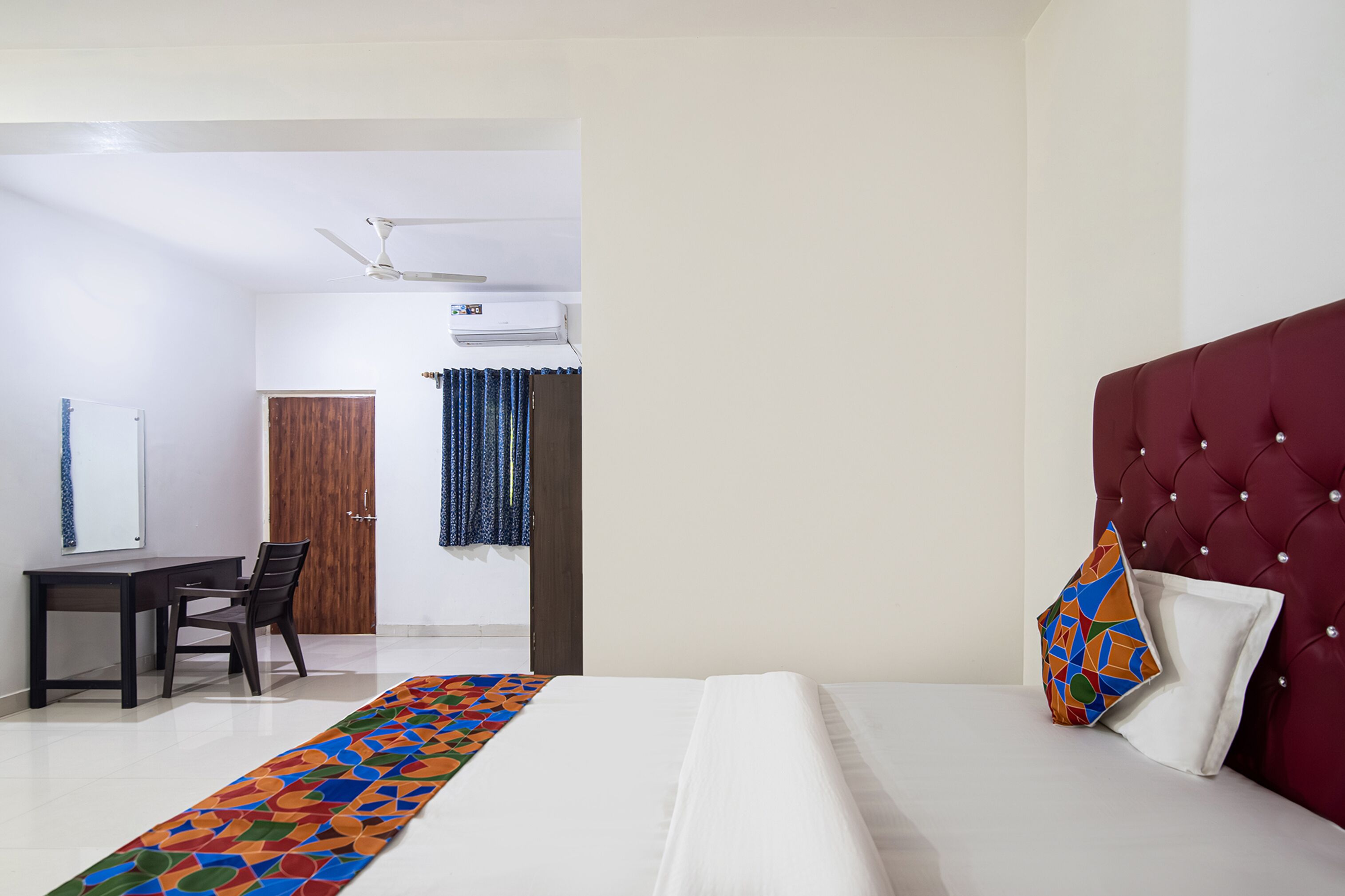 Una habitación de hotel con una cama, un escritorio, una silla, un armario y un ventilador de techo.