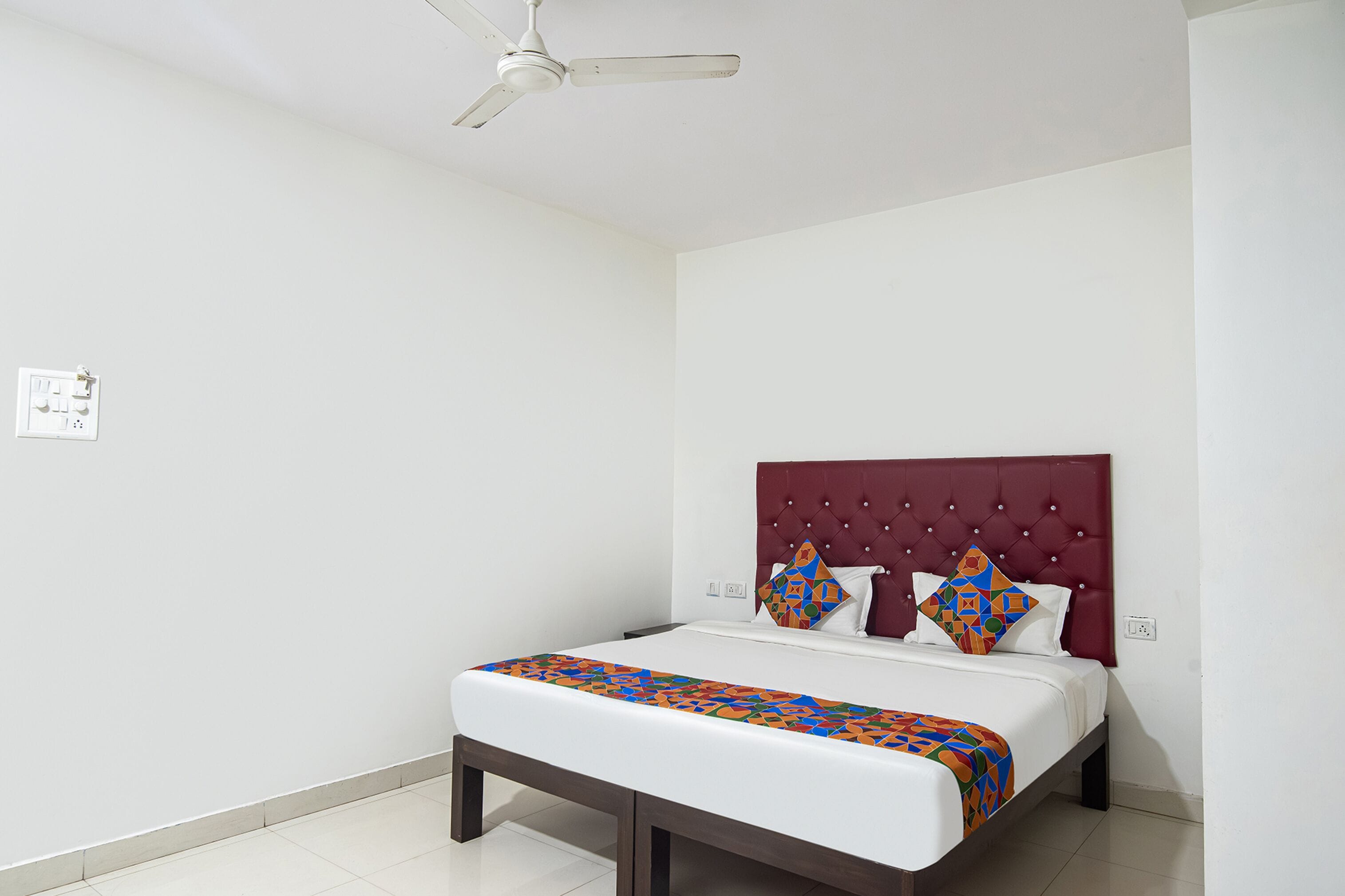 A neatly made bed with a colorful geometric-patterned bedspread, a tufted headboard, and two decorative pillows.