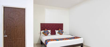Un dormitorio con puerta de madera, cama con cabecera roja, ropa de cama blanca y una manta colorida.