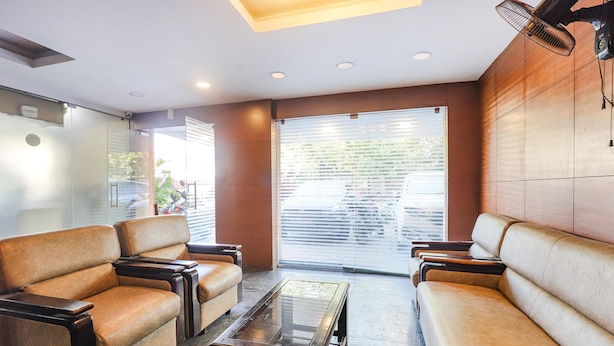 A modern waiting area with leather sofas, a glass-top coffee table, and a large sliding glass door leading to an outdoor area. - Fabhotel Ample Yard (Chennai)