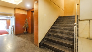 A staircase with a handrail, a potted plant, and a red carpet leading to an entrance. - Fabhotel Ample Yard (Chennai)