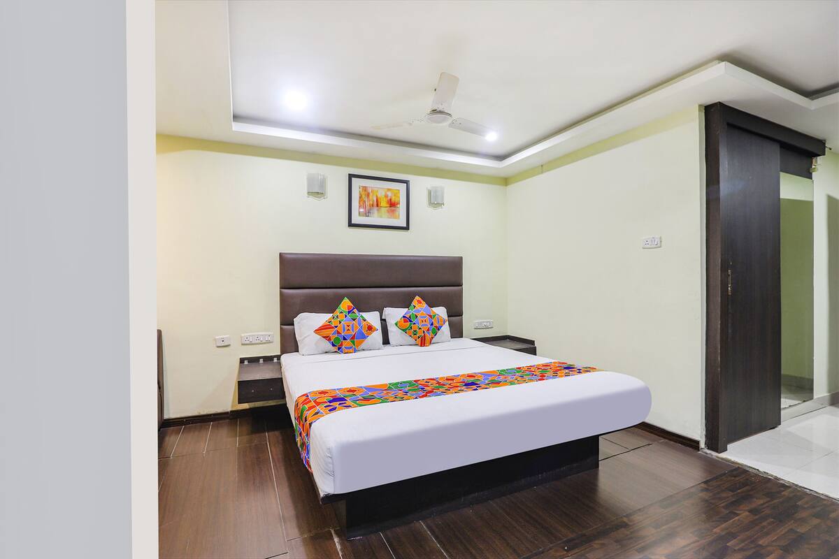 Une chambre à coucher avec un lit, une tête de lit, un ventilateur de plafond, une table de chevet et une porte.
