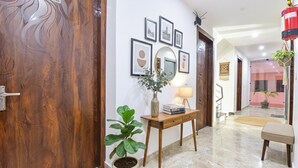 A modern hallway with a wooden door, a potted plant, a small wooden table with a lamp, and framed pictures on the wall. - Fabhotel Hari Residency (Haridwar)