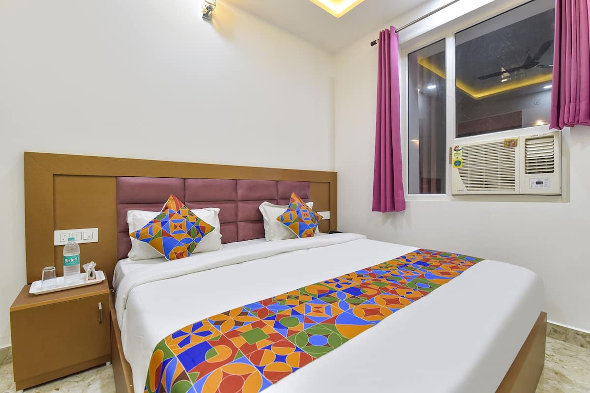 A hotel room with a bed, a nightstand, a window with curtains, and an air conditioning unit.