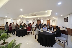 Une salle de conférence équipée de tables rondes, de chaises et accueillant des participants.