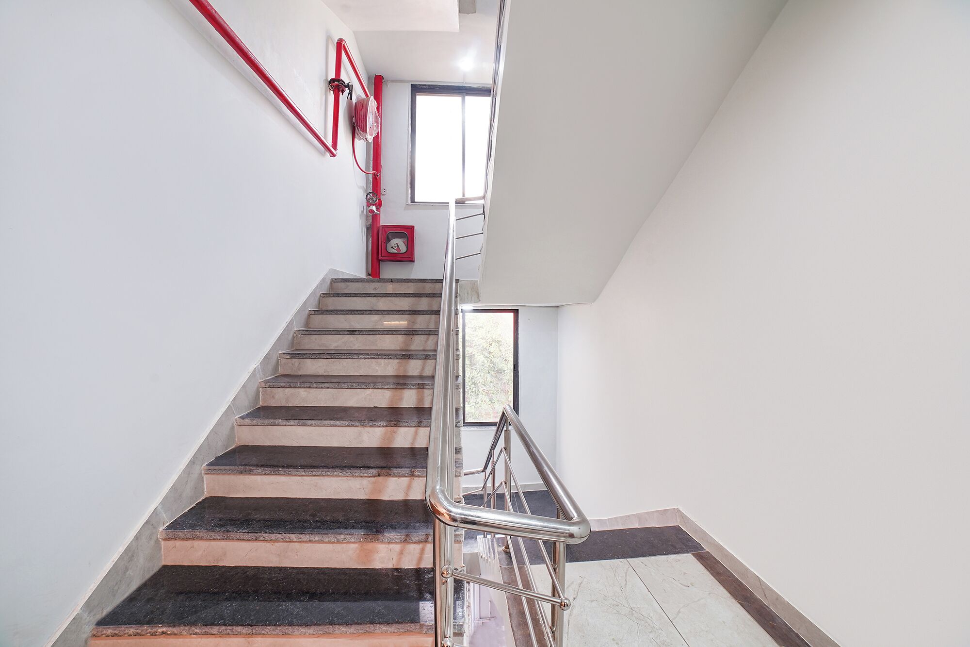 A staircase with a metal handrail, a fire alarm, and a window at the top.