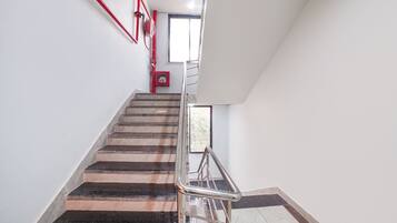 A staircase with a metal handrail, a fire alarm, and a window at the top.
