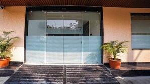 Une entrée d’immeuble avec une porte coulissante en verre, un plafond en bois et deux plantes en pot de chaque côté.