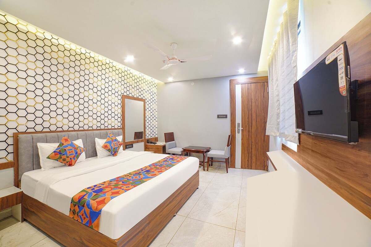 A modern hotel room with a large bed, a wooden headboard, a mirror, a desk, a chair, and a TV mounted on the wall.
