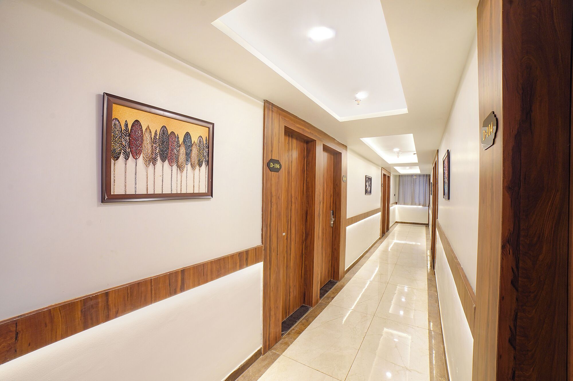 A hotel hallway with wooden doors, a framed artwork on the wall, and a sign indicating room number D-106.