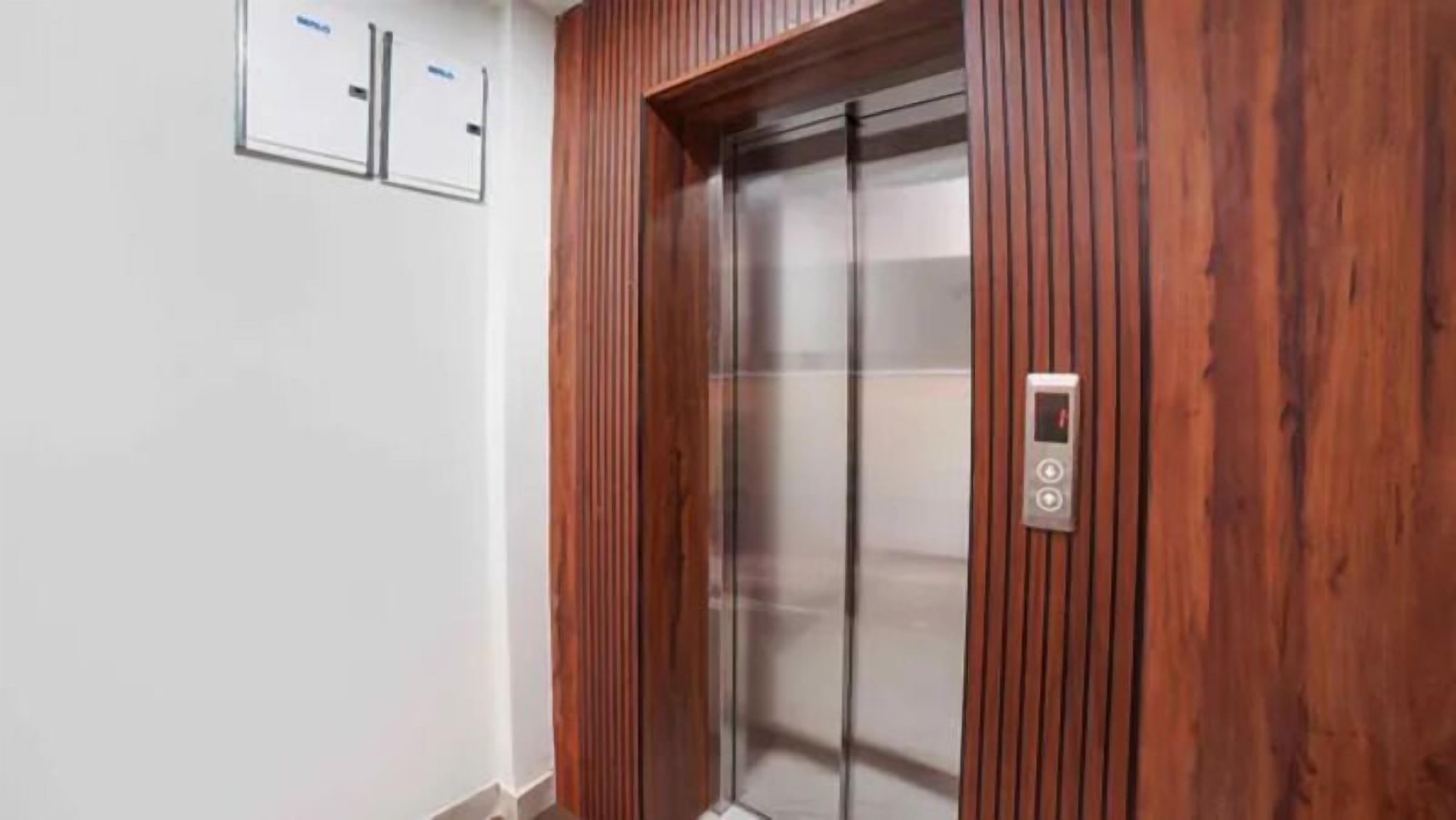 A modern elevator with a wooden panel design, a control panel, and a clear glass door.