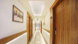 Un couloir d’hôtel avec des portes en bois, une œuvre d’art encadrée sur le mur de gauche et un luminaire au plafond.
