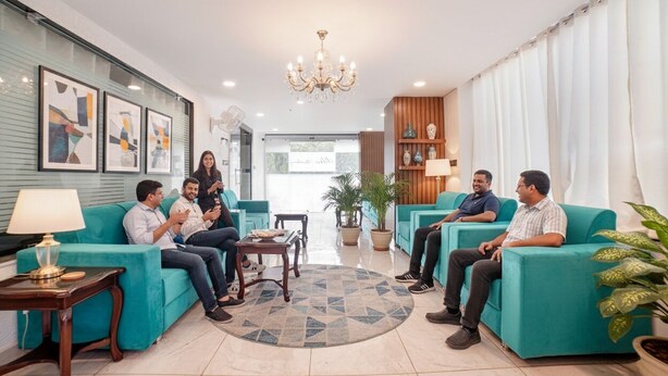 Un espace de détente moderne avec des canapés turquoise, un lustre et des œuvres d’art encadrées accrochées aux murs.