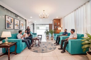 A modern lounge area with teal sofas, a chandelier, and framed artwork on the walls. - FabHotel Prime Bliss Residency - ISBT (Bhopal)