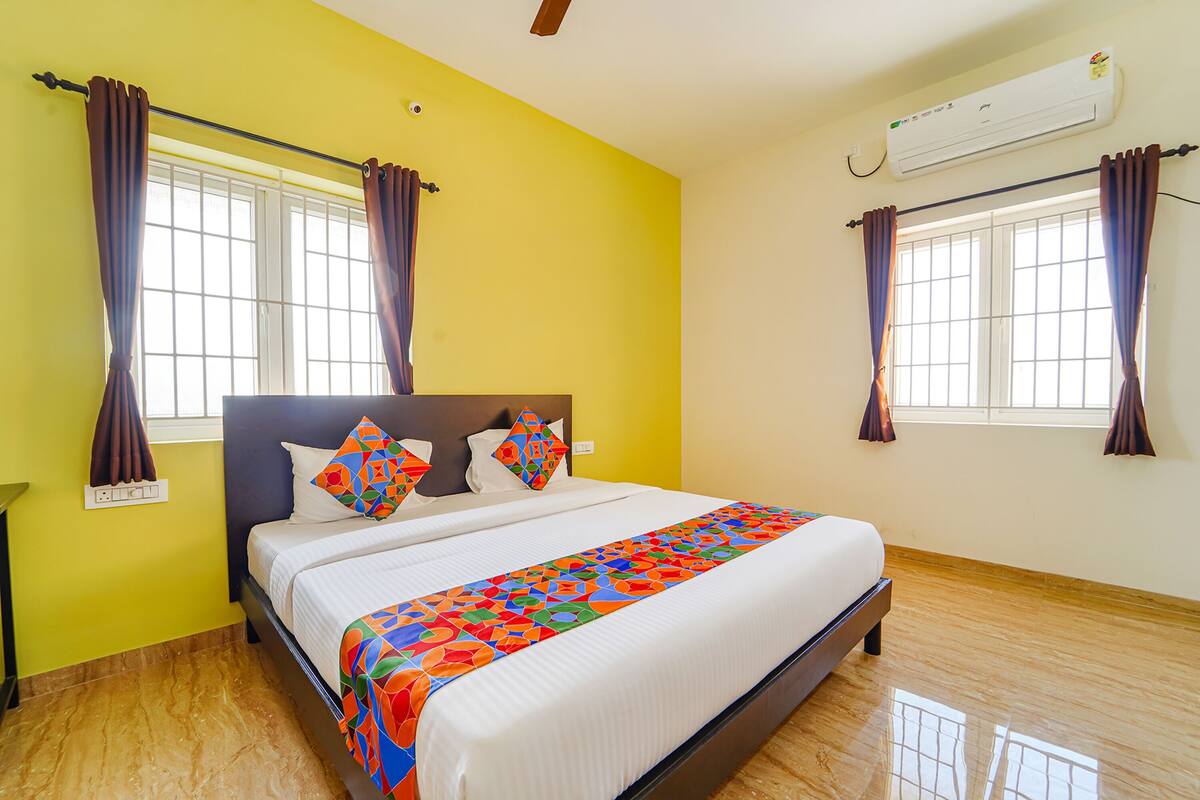 Une chambre d’hôtel avec un grand lit, deux fenêtres avec des rideaux, un ventilateur de plafond et un appareil de climatisation.