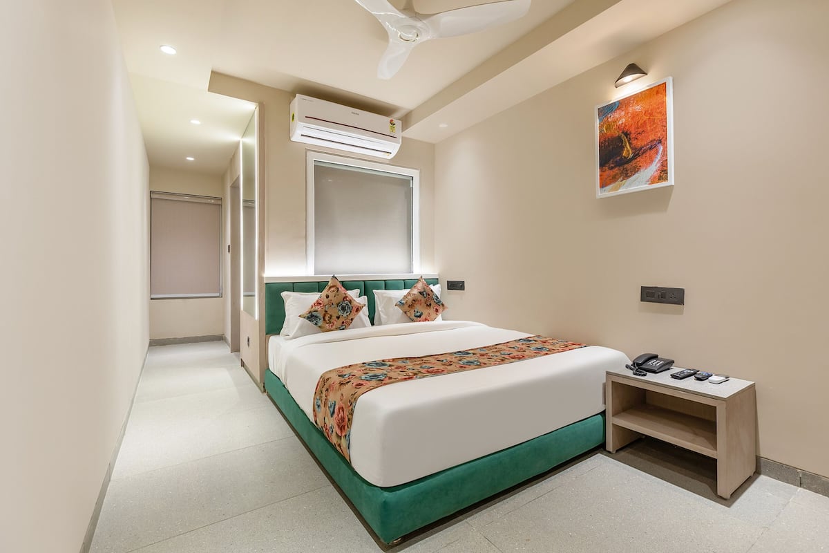 Una habitación de hotel con una cama, una mesita de noche, un equipo de aire acondicionado y un cuadro en la pared.