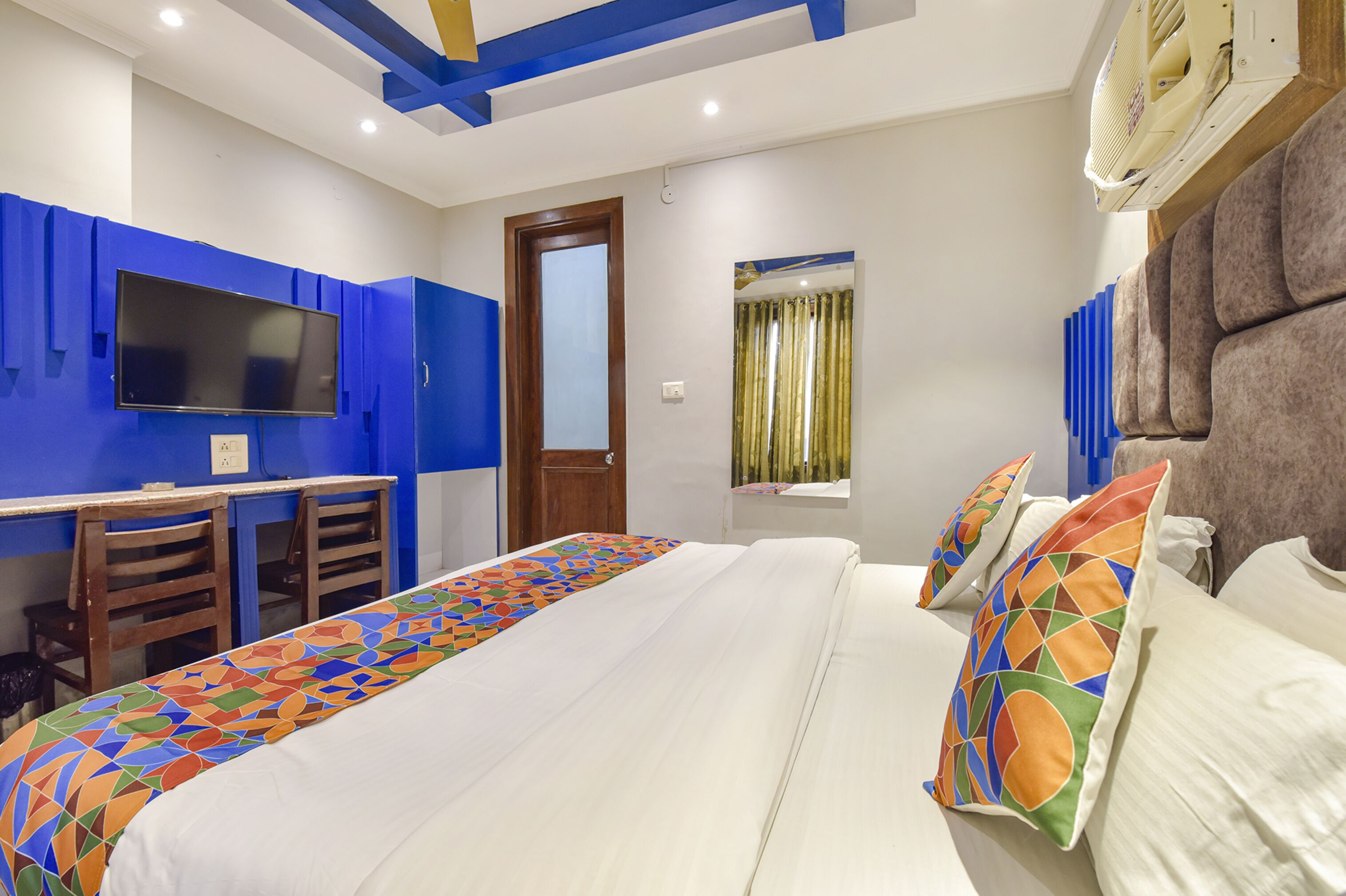 A hotel room with a bed, a desk with two chairs, a television, and a window with curtains.