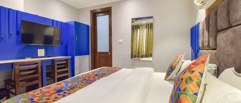 A hotel room with a bed, a desk with two chairs, a television, and a window with curtains.