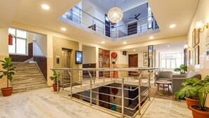 Un vestíbulo amplio con piso de mármol, piscina con barandilla de cristal, una escalera y un entrepiso con candelabro.
