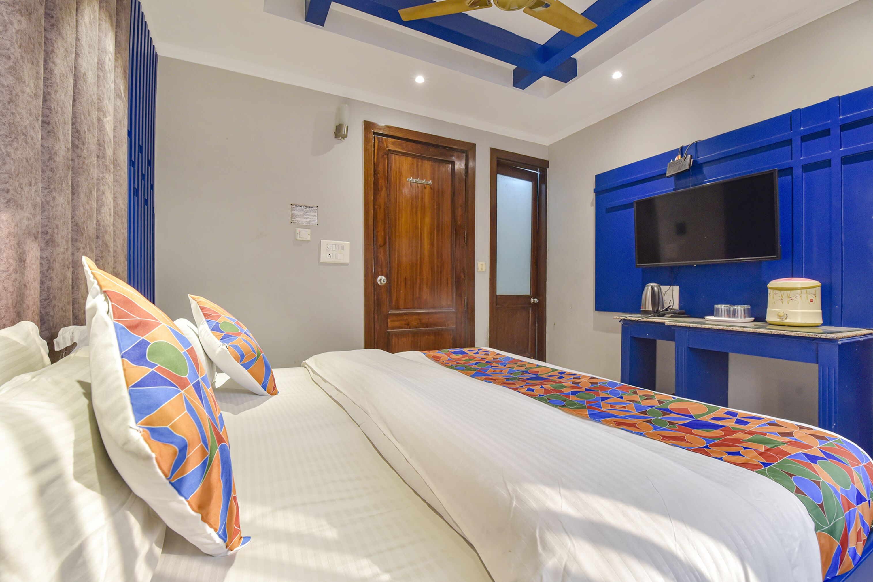 A hotel room with a bed, pillows, a TV, and a desk with a kettle.