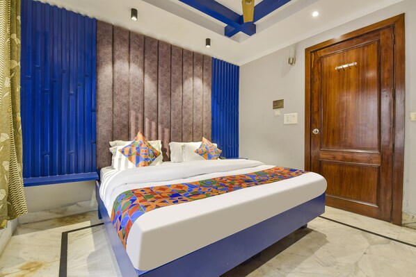 A bedroom with a large bed, blue curtains, a wooden door, and a patterned bedspread.