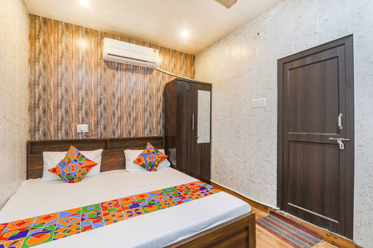 A bedroom with a wooden headboard, a bed with colorful pillows, a striped rug, and a dark wooden door.