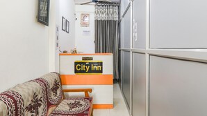 A reception area with a reception desk labeled "City Inn," a ceiling fan, a check-out sign, and a patterned sofa. - Fabexpress City Inn (Faizabad)