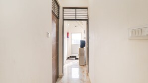 A hallway with a tiled floor, a door with a metal frame, and a wall-mounted light switch. - Fabexpress City Inn (Faizabad)