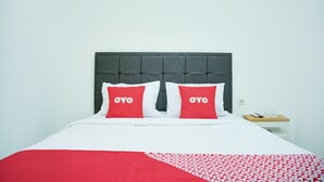 A bed with a dark headboard, two pillows with "OYO" text, a white and red bedspread, and a small bedside table with a phone and a cup. - Hotel O Teluk Betung Near Water Park Lembah Hijau Formerly Kanajiwa Guesthouse 2 (Bandar Lampung)