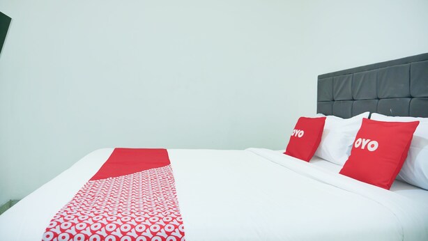 A neatly made bed with a white and red patterned bedspread, two red pillows with the word "YOYO" on them, and a grey upholstered headboard. - Hotel O Teluk Betung Near Water Park Lembah Hijau Formerly Kanajiwa Guesthouse 2 (Bandar Lampung)