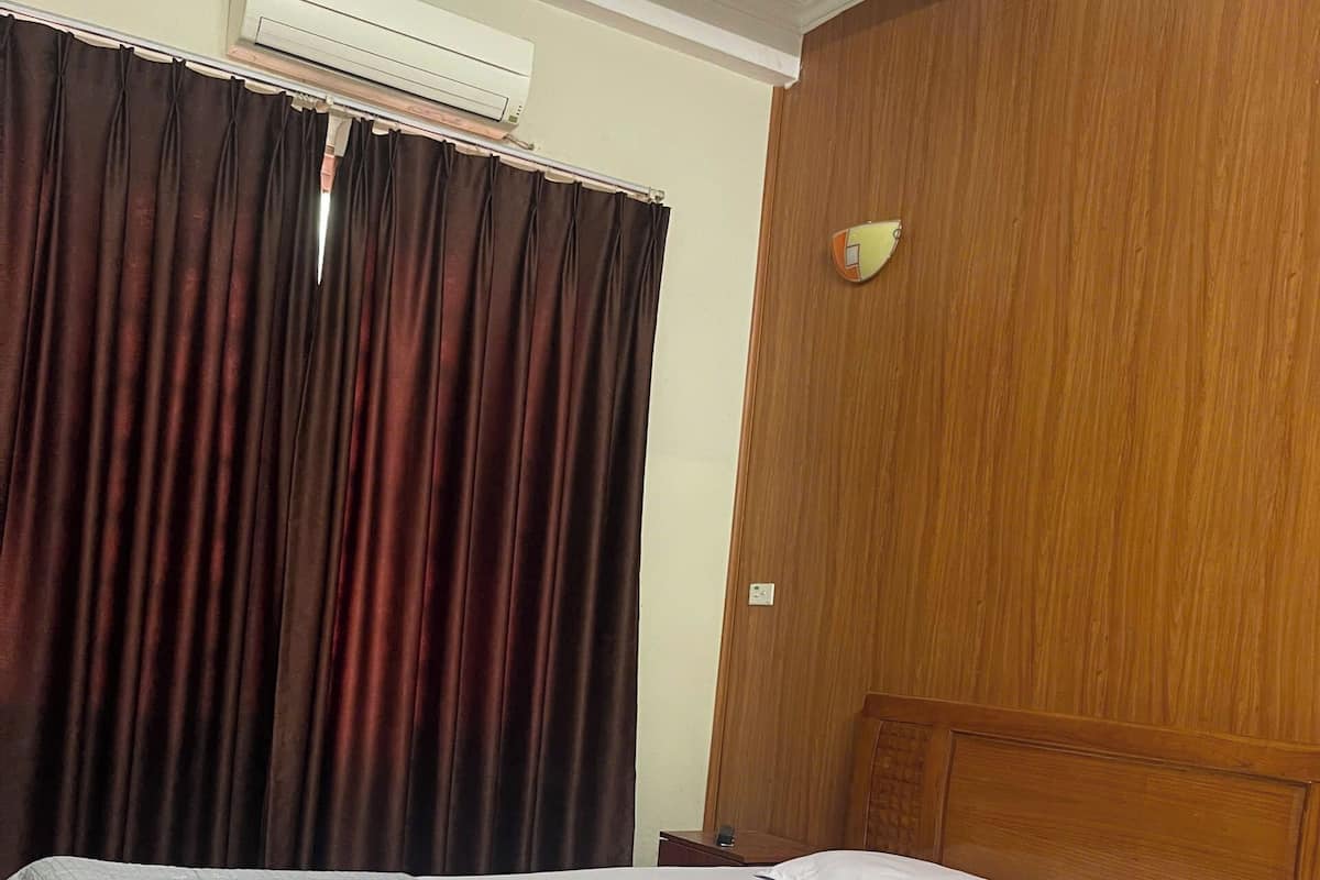 Une chambre d’hôtel avec un lit, des rideaux, un appareil de climatisation et une tête de lit en bois.