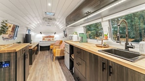 A compact, modern RV kitchen with a wooden countertop, a sink, and a window offering a view of greenery.