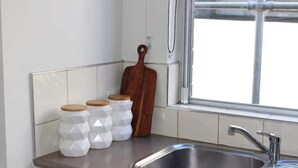 Une cuisine dotée d’un évier en acier inoxydable, de pots à épices hexagonaux blancs, d’une planche à découper en bois et d’une fenêtre offrant une vue agréable.