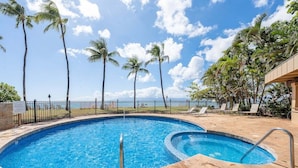 A swimming pool with a curved design, surrounded by palm trees and a clear sky.